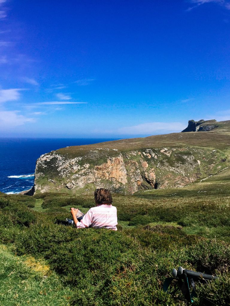 Turista tra la vegetazione costiera con vista sul mare aperto, trekking in Irlanda