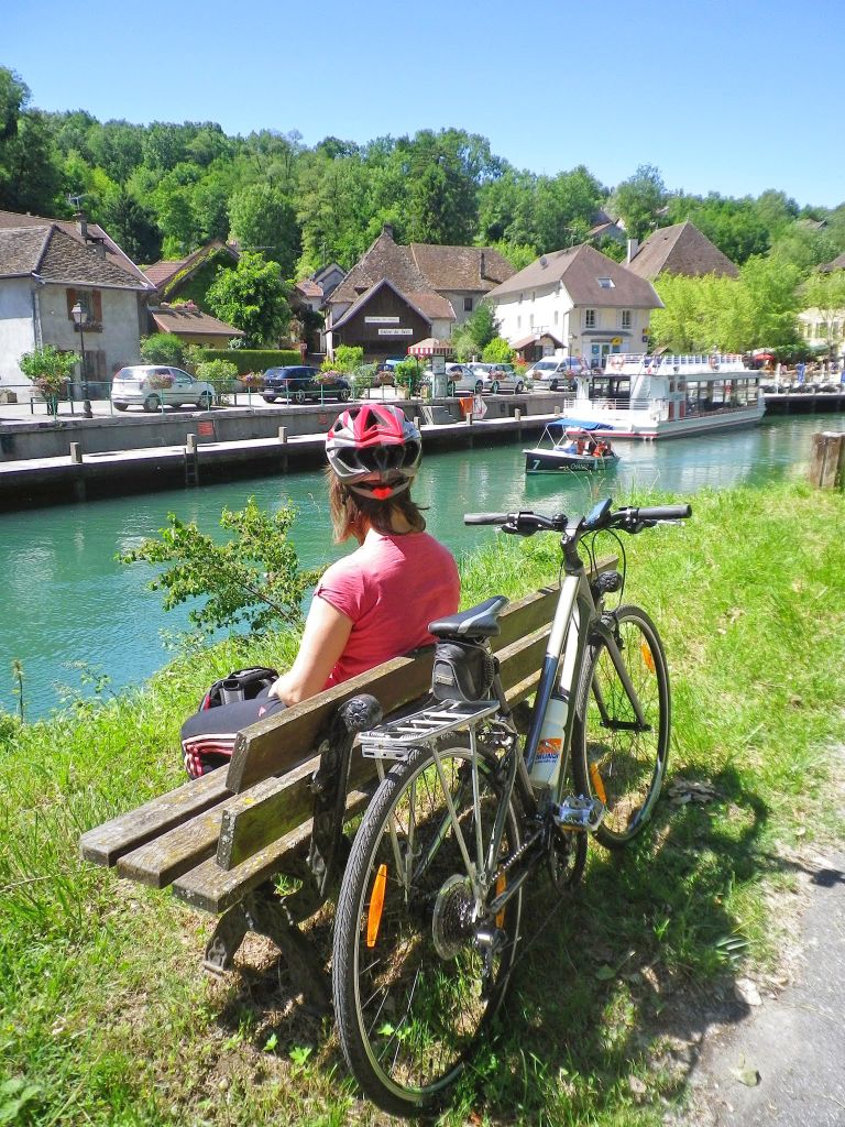 Ciclista seduto su una panchina lungo un canale verdeggiante, in un’area rurale vicino a Ginevra.