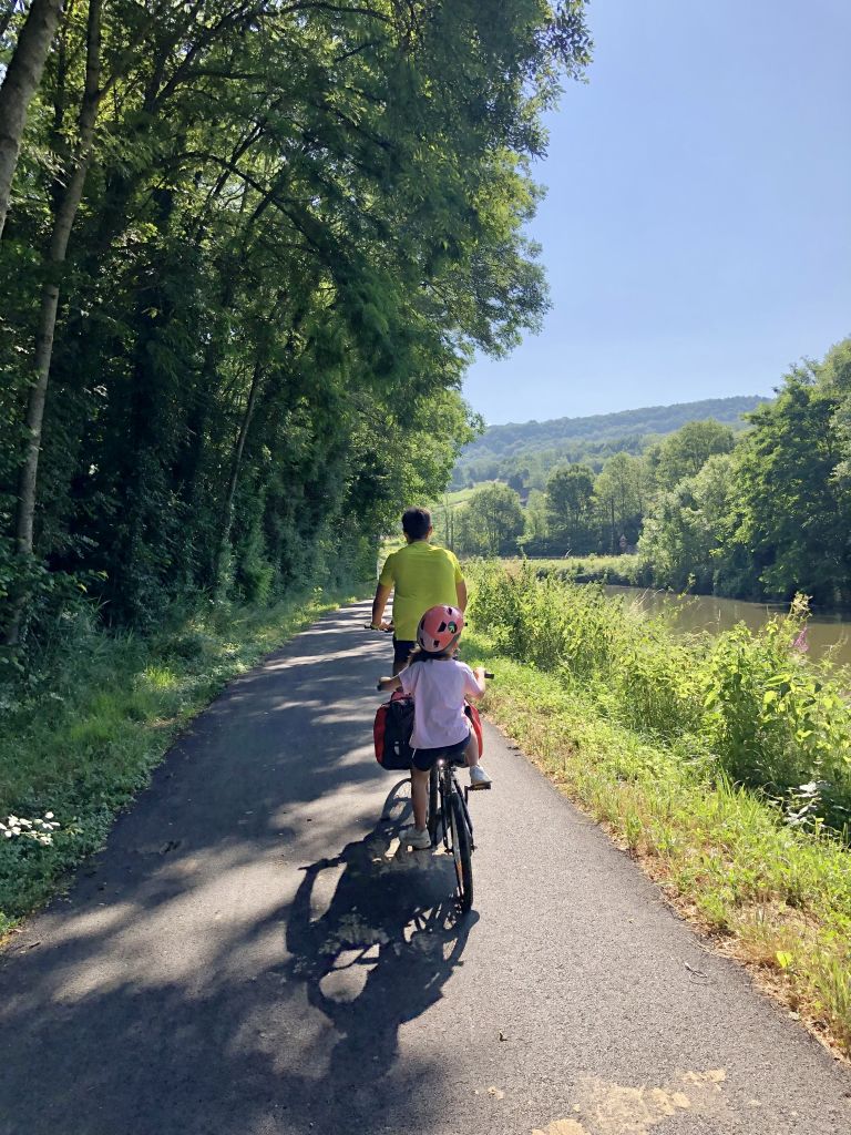 Famiglia in bici su pista ciclabile circondata da alberi verdi lungo il fiume, vacanze in bici per famiglie, Francia