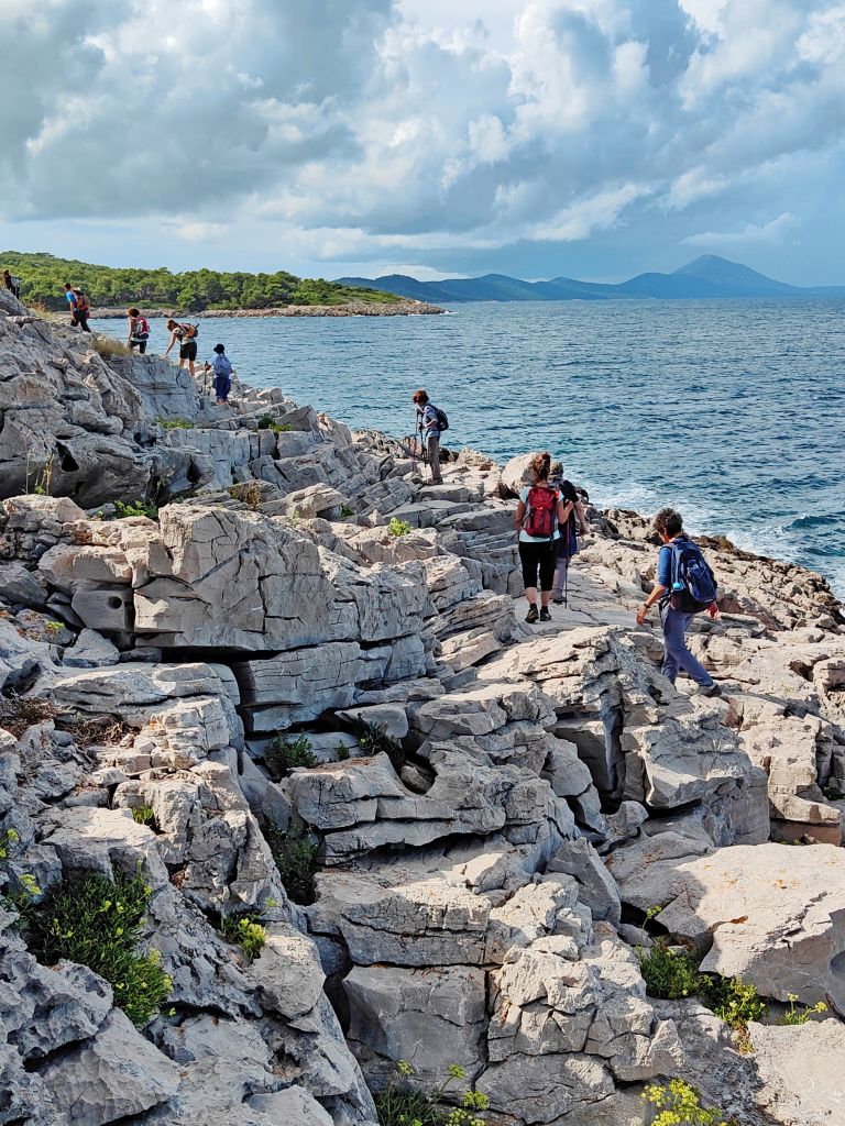Escursionisti in cammino su sentiero costiero su rocce vicino al mare, trekking in Croazia