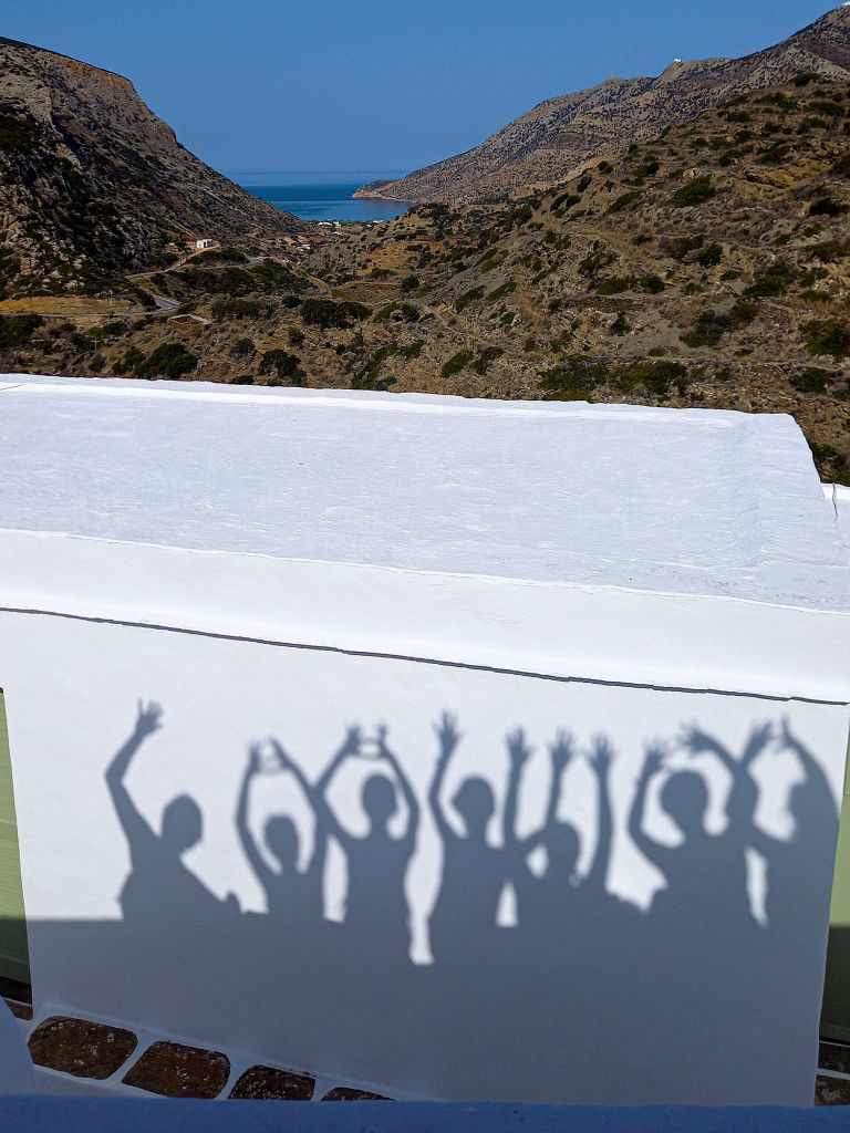 Ombre di camminatori proiettate su un muro bianco a Sifnos.