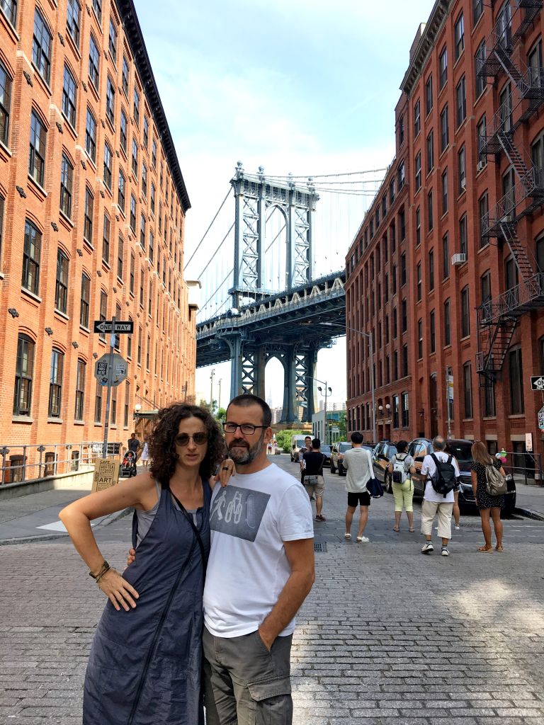 Coppia in posa tra edifici di mattoni rossi con il Manhattan Bridge sullo sfondo.