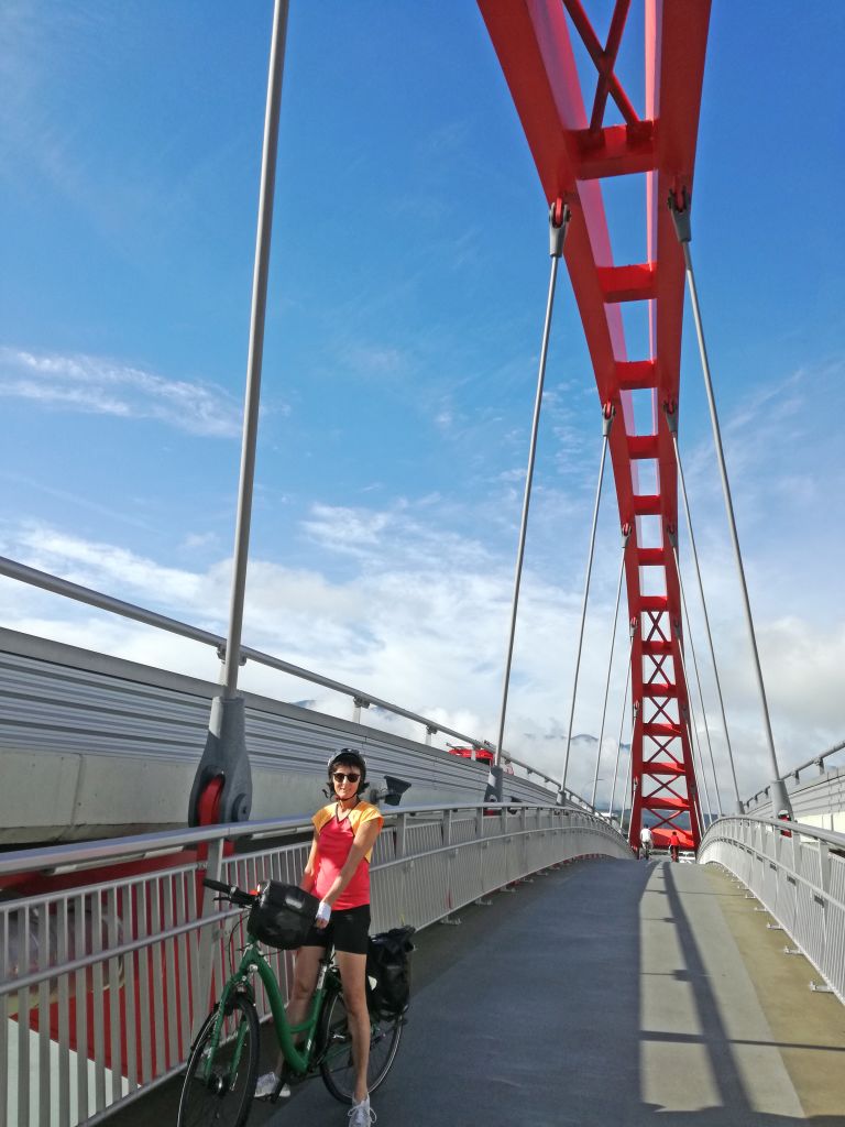 Ciclista su un ponte rosso con vista panoramica sul lago Wörthersee, Carinzia.
