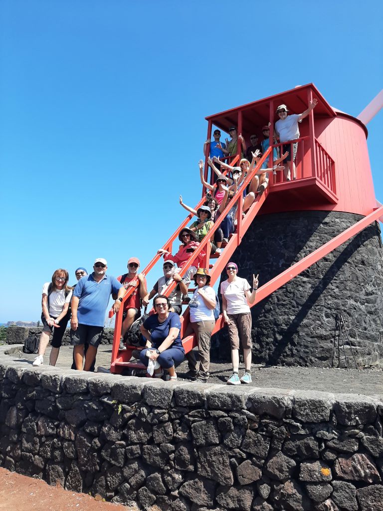 Gruppo di turisti in viaggio con Girolibero in posa davanti a un mulino rosso, Isole Azzorre, Portogallo.