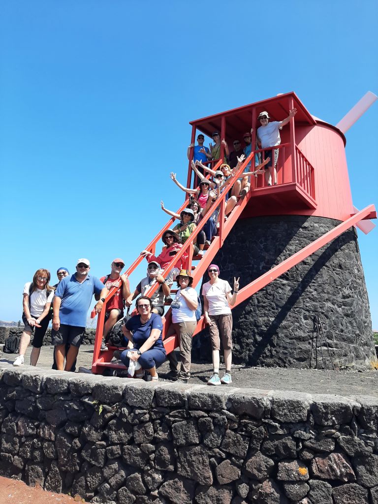 Gruppo di persone in viaggio con Girolibero in visita a un mulino tradizionale con struttura in pietra e scala rossa nelle Azzorre.