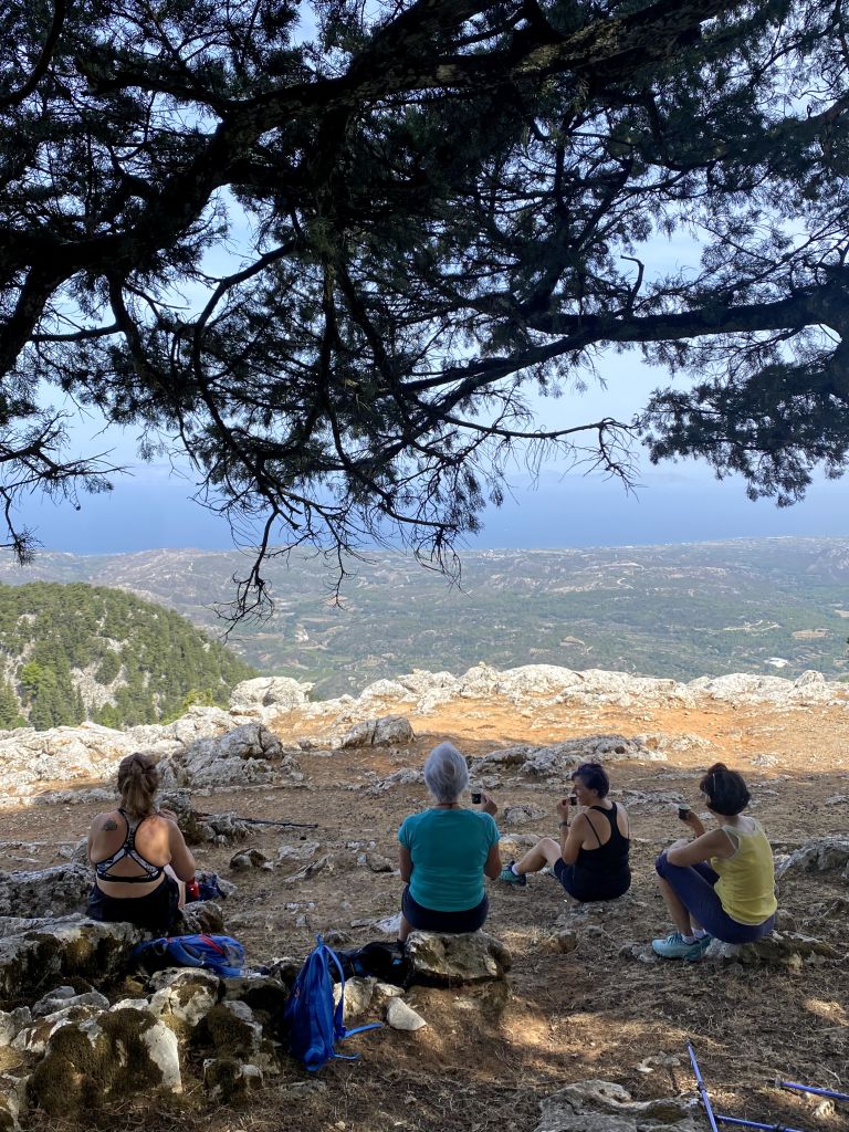 Trekker in viaggio in gruppo con Girolibero che si riposano all’ombra di un albero sul Monte Attavyros, con vista panoramica su Rodi, Grecia.