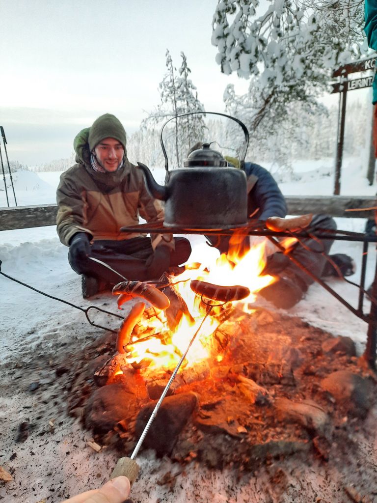 Persone che cuociono cibo sul fuoco all'aperto durante un'escursione in Lapponia, Finlandia.