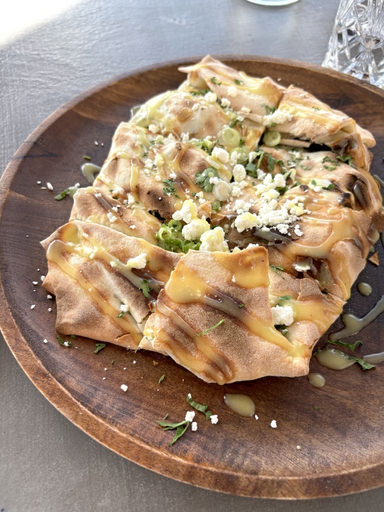 Piatto tradizionale greco con pita ripiena e formaggio locale su tavola rustica.