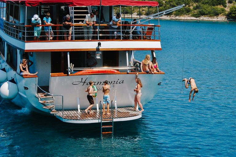 Barca "Harmonia" al largo della costa croata con persone che si tuffano in mare e altre che si rilassano nel ponte superiore