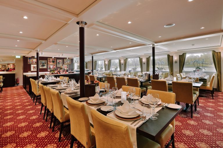 Ampia sala da pranzo con finestre panoramiche e tavoli imbanditi su nave da crociera fluviale in Europa.