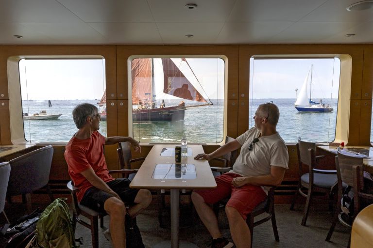 Paar sitzt am Tisch im Inneren des Bootes mit Fenstern mit Blick auf das Meer