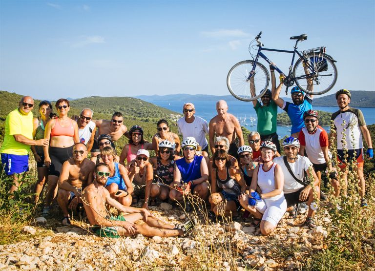 Group of smiling cyclists on a scenic hill overlooking the sea, Croatia, boat bike trips