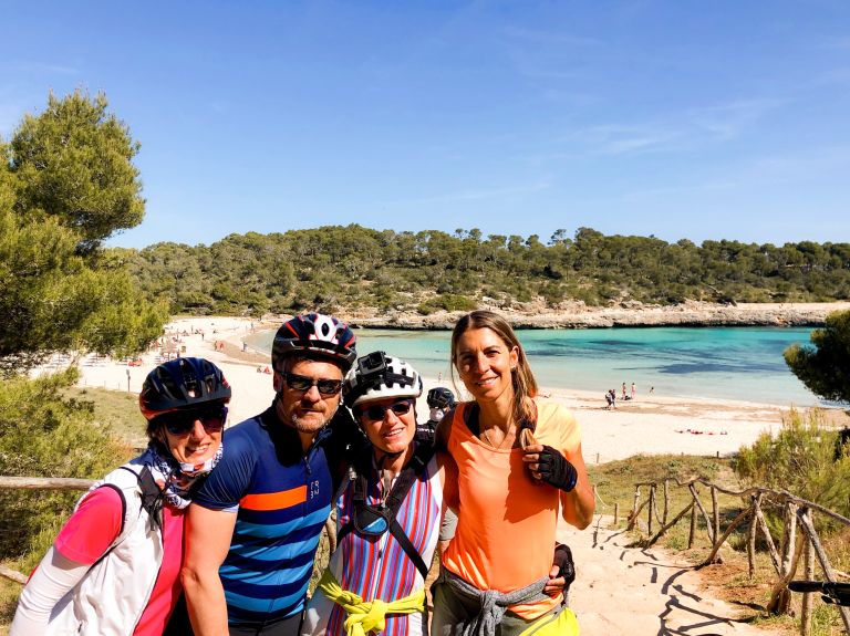 Gruppo di amici sorridenti con il mare sullo sfondo a Maiorca, vacanze in bici 
