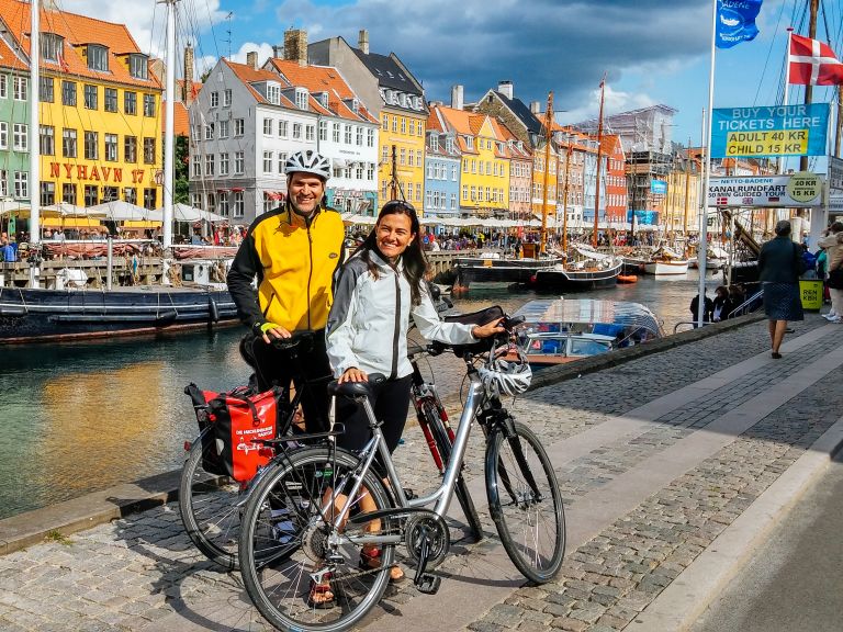 Coppia di ciclisti sorridenti nel quartiere di Nyhavn con le sue case colorate lungo il canale, Copenaghen, Danimarca