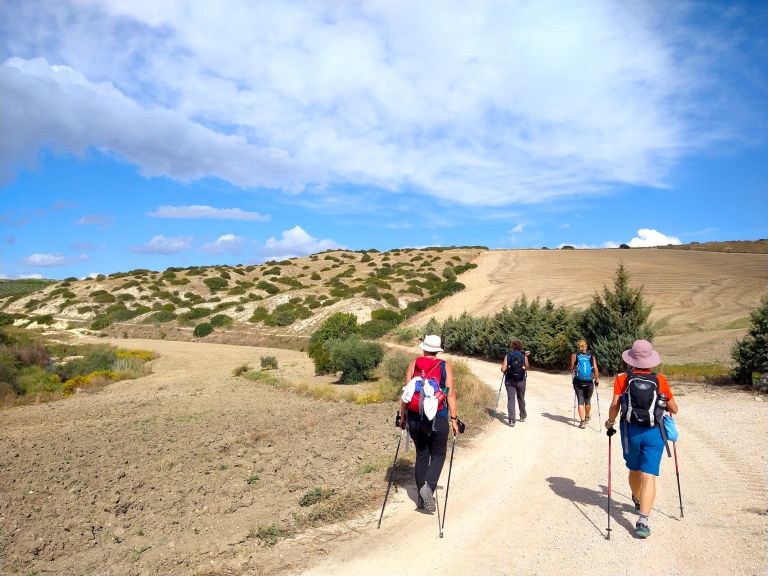 Pellegrini che camminano su un sentiero sabbioso tra colline aride sul Cammino Materano.