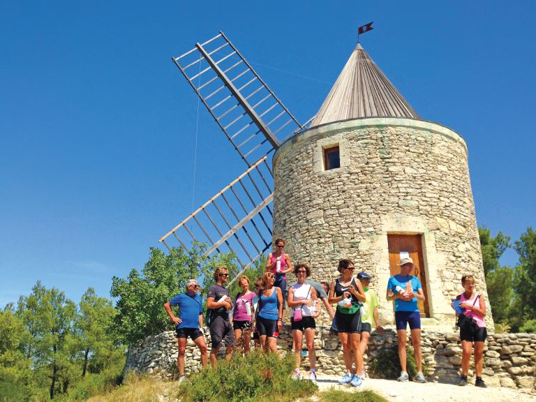Gruppo davanti a un mulino a vento storico in un paesaggio collinare durante un viaggio in Provenza.