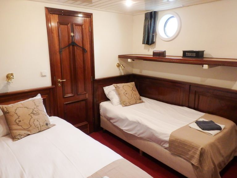 cabin with twin beds, porthole, and wood accents on a river cruise ship in Europe.