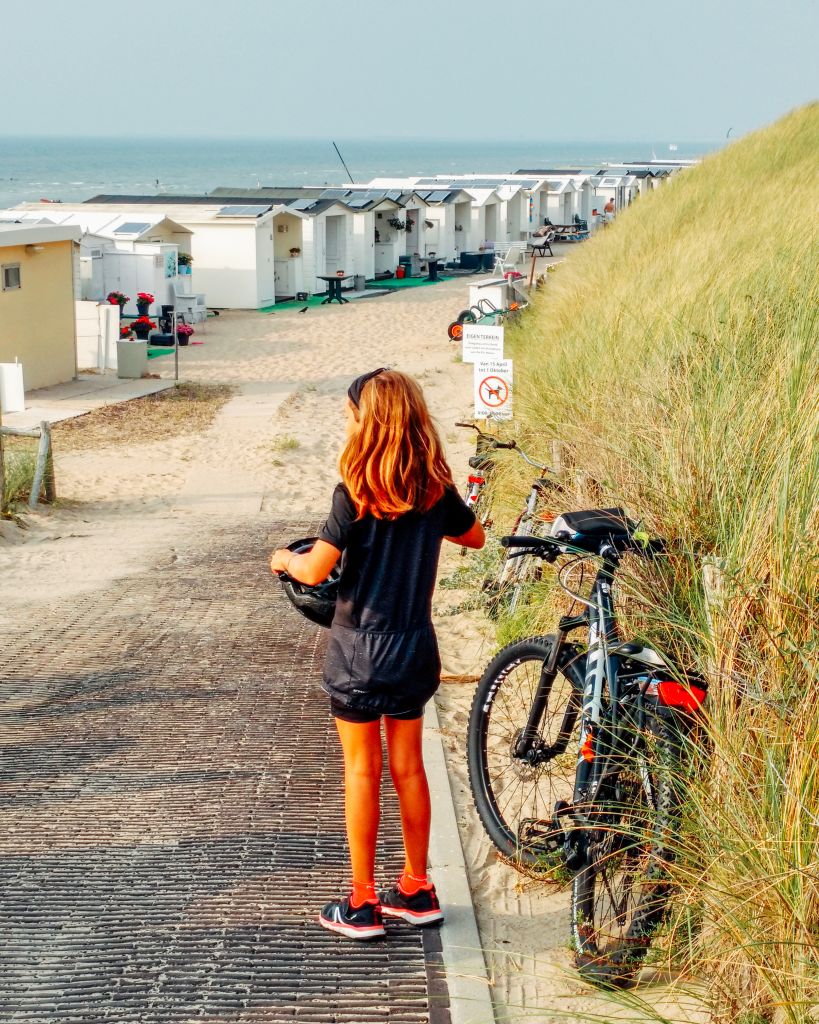 Bambina con bicicletta lungo una spiaggia sulla costa olandese, viaggi in bici per famiglie