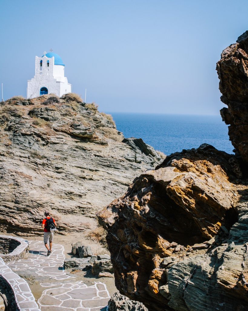 Escursionista su sentiero costiero, Cappella bianca di Panagia Poulati con vista sul mare, Sifnos, Grecia