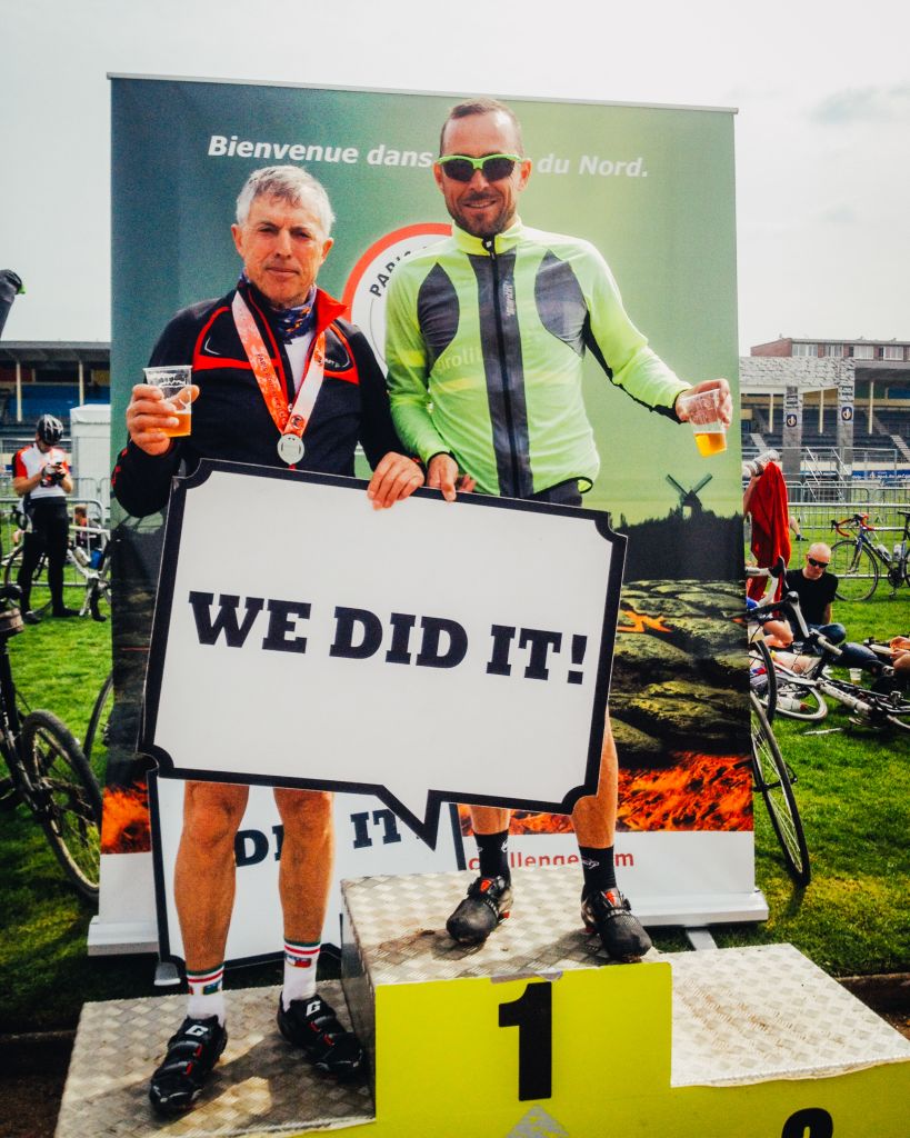 Due ciclisti in posa sul podio con cartello "We did it", gara ciclistica, granfondo Parigi Roubaix