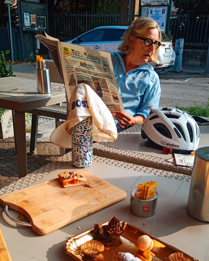 Donna in viaggio con Girolibero che si gode una pausa pranzo con pizza e snack su un tavolo all’aperto durante un viaggio in bici.