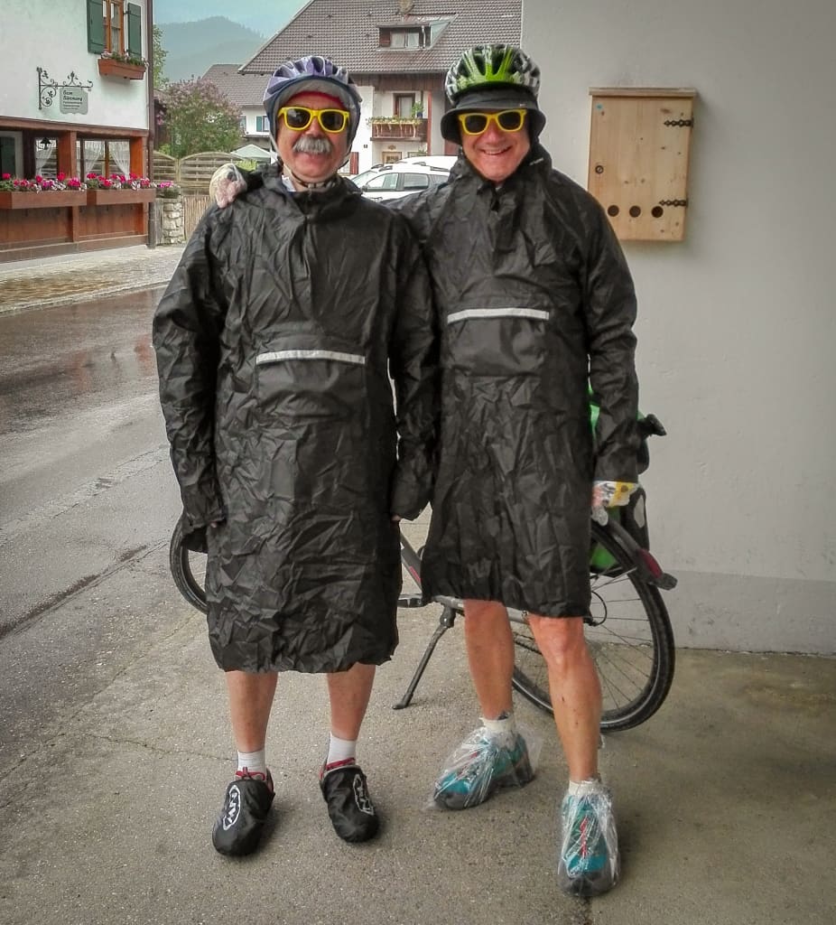 Due ciclisti sorridenti con impermeabile per proteggersi dalla pioggia