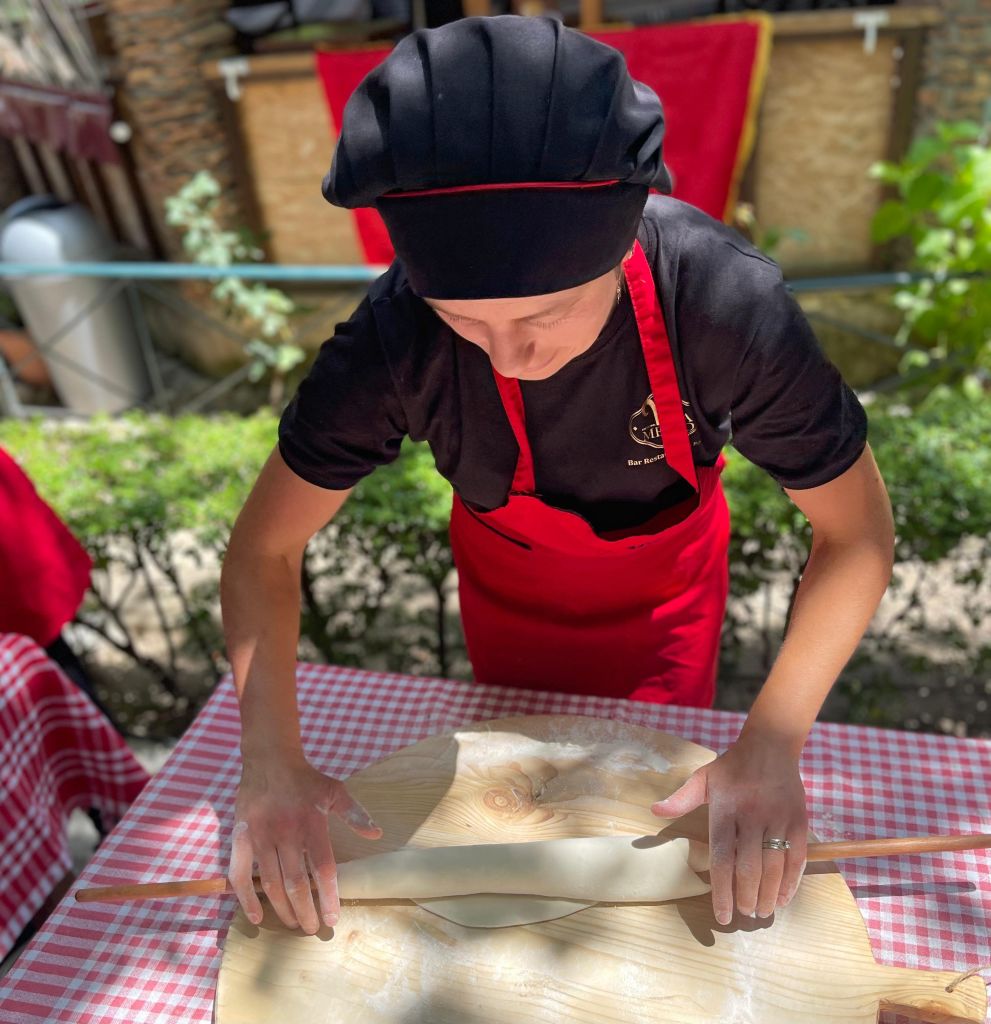 Donna albanese che prepara pane tradizionale in un forno a legna.