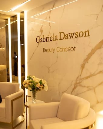 Recepção da clínica com o nome Gabriela Dawson Beauty Concept aplicado em parede de mármore, poltronas claras e arranjo de flores