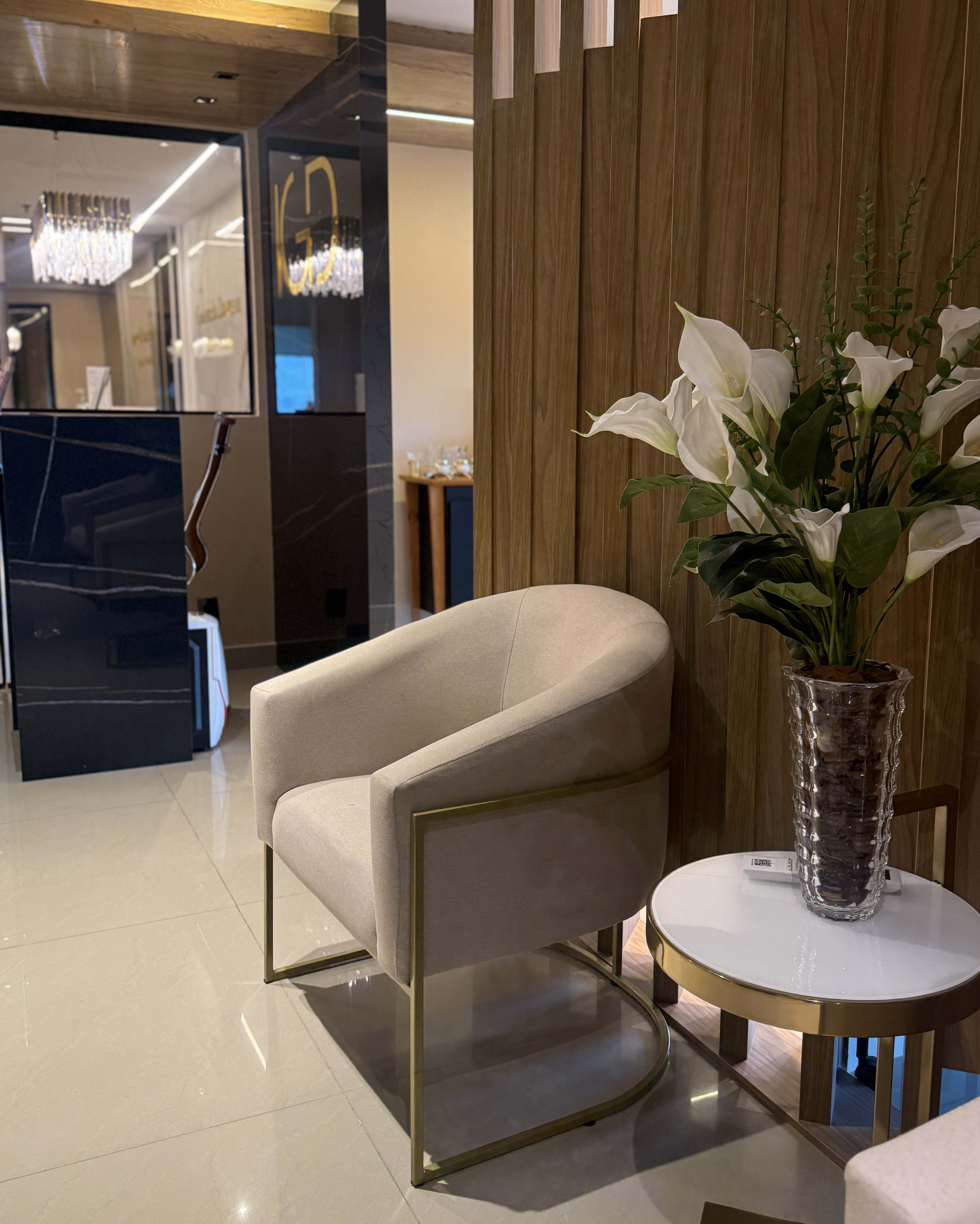 Sala de espera da clínica com poltrona clara, mesa lateral de mármore e painel de madeira ripada