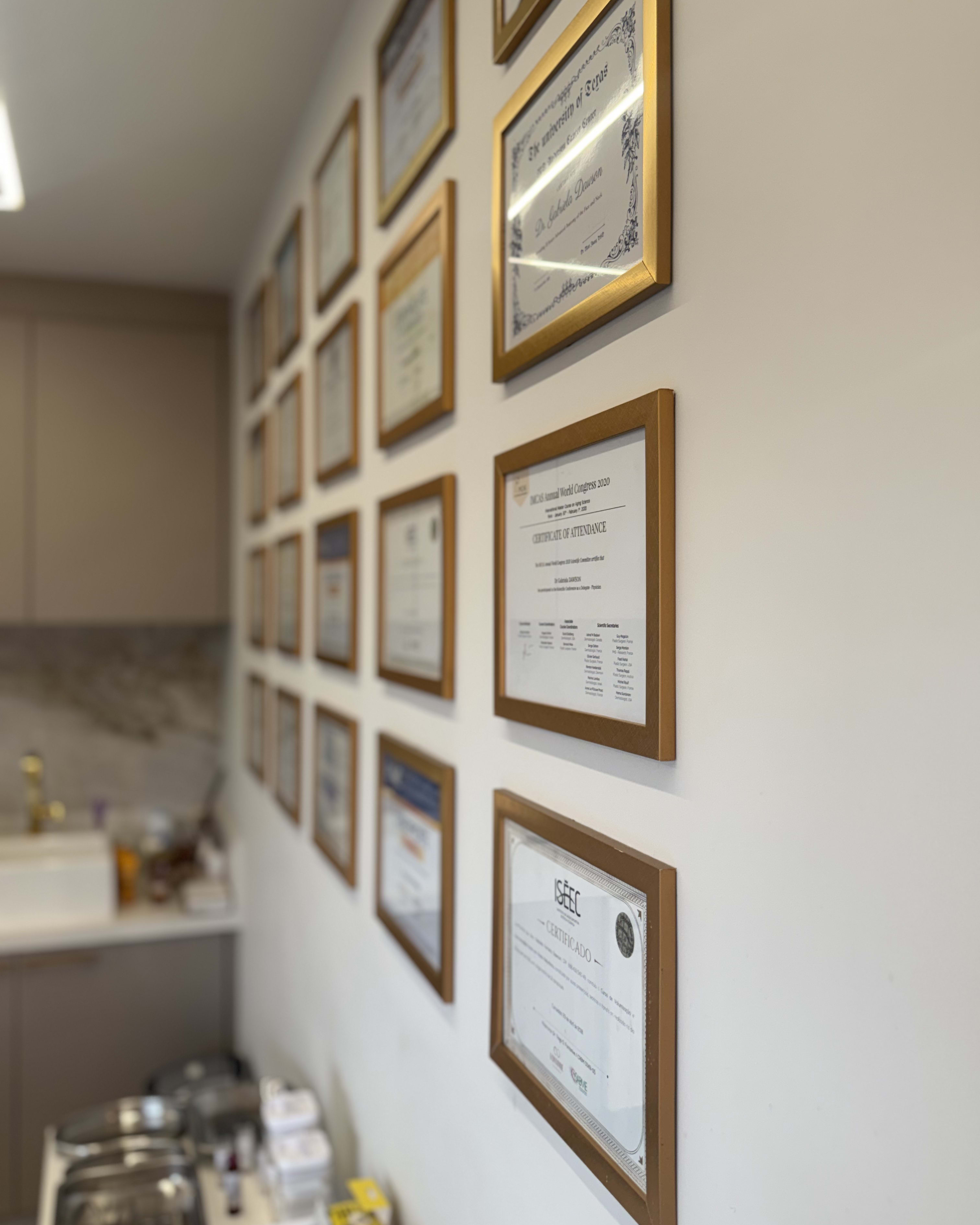 Parede da clínica com diplomas e certificados de formação emoldurados, vistos em perspectiva
