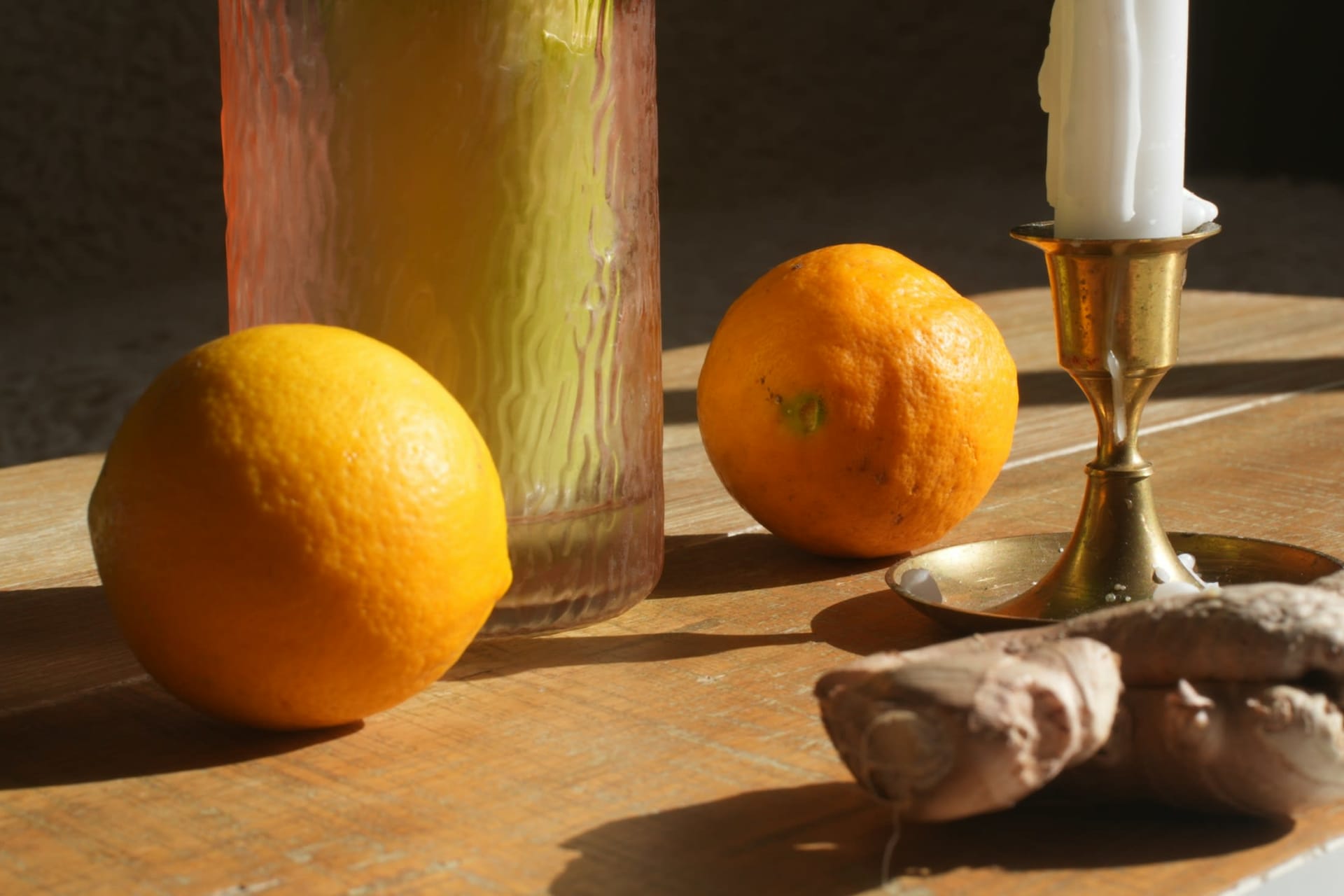 Fresh oranges beside a white candle in a brass holder in warm afternoon sunlight