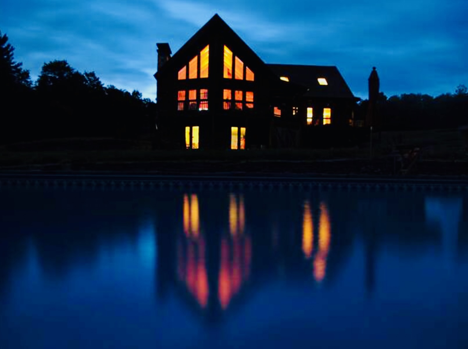 Mountain Meadows chalet glowing at night reflected in pool Catskills wedding venue Long Eddy NY