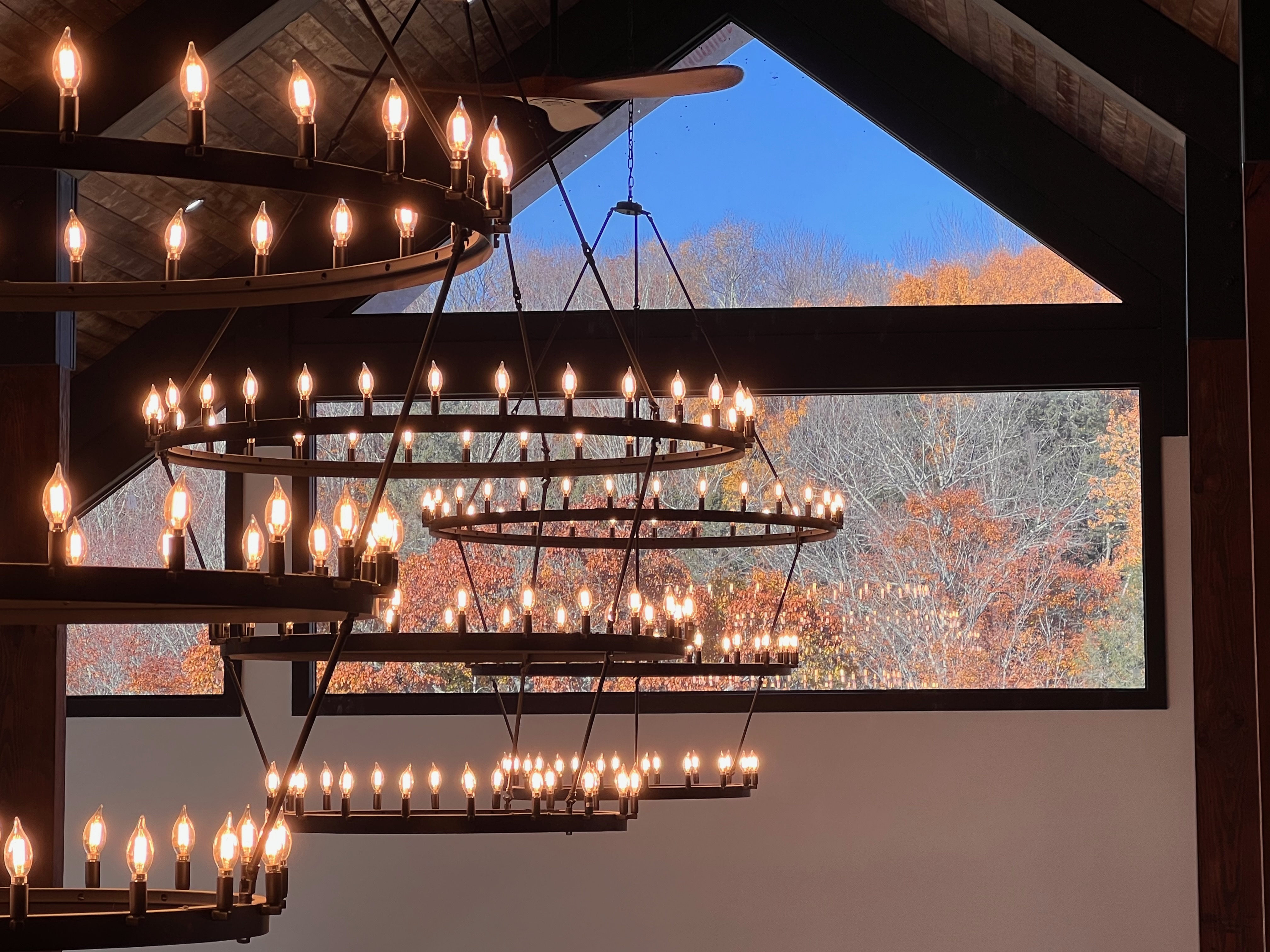 Dramatic chandeliers with fall foliage through barn windows at Mountain Meadows Catskills wedding venue