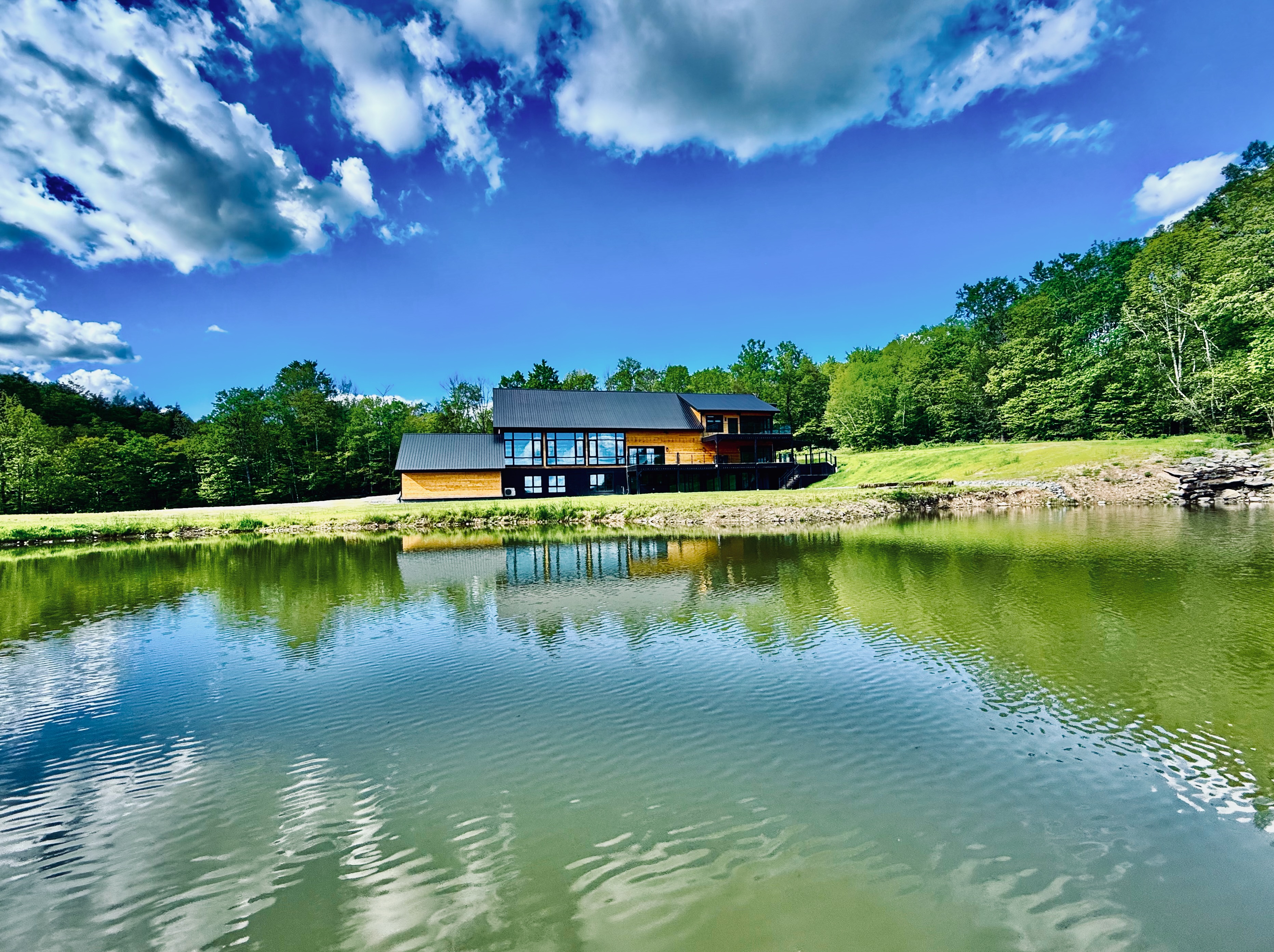 Mountain Meadows modern barn and lodge reflected in pond on blue sky day Catskills wedding venue Long Eddy NY