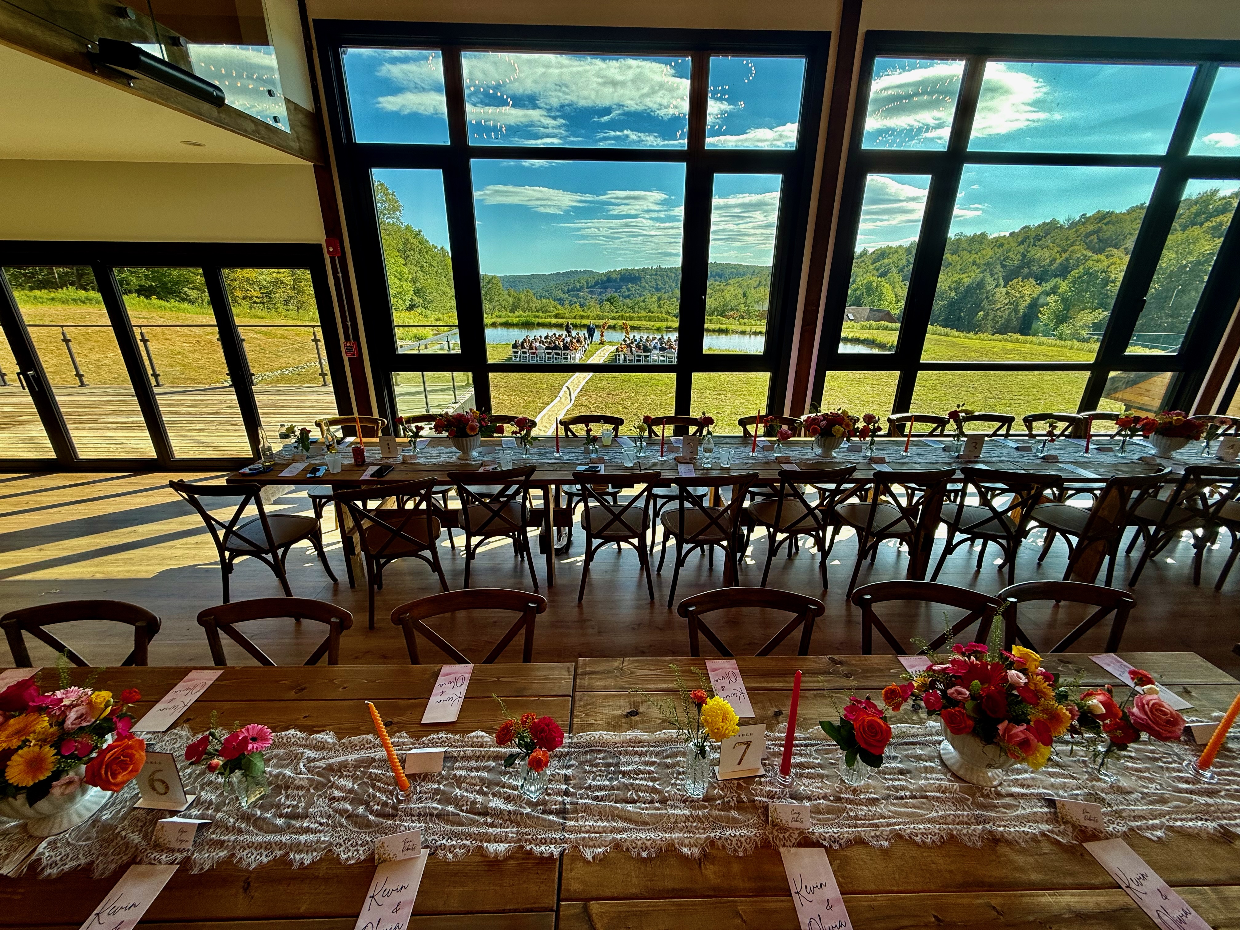Barn wedding reception tables with outdoor ceremony visible through panoramic windows at Mountain Meadows Catskills venue