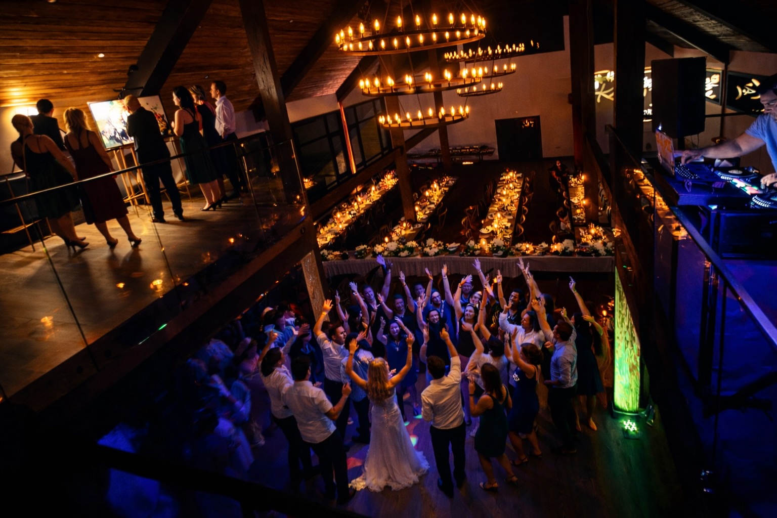Wedding reception dance floor photographed from mezzanine with chandeliers and DJ at Mountain Meadows Catskills barn venue