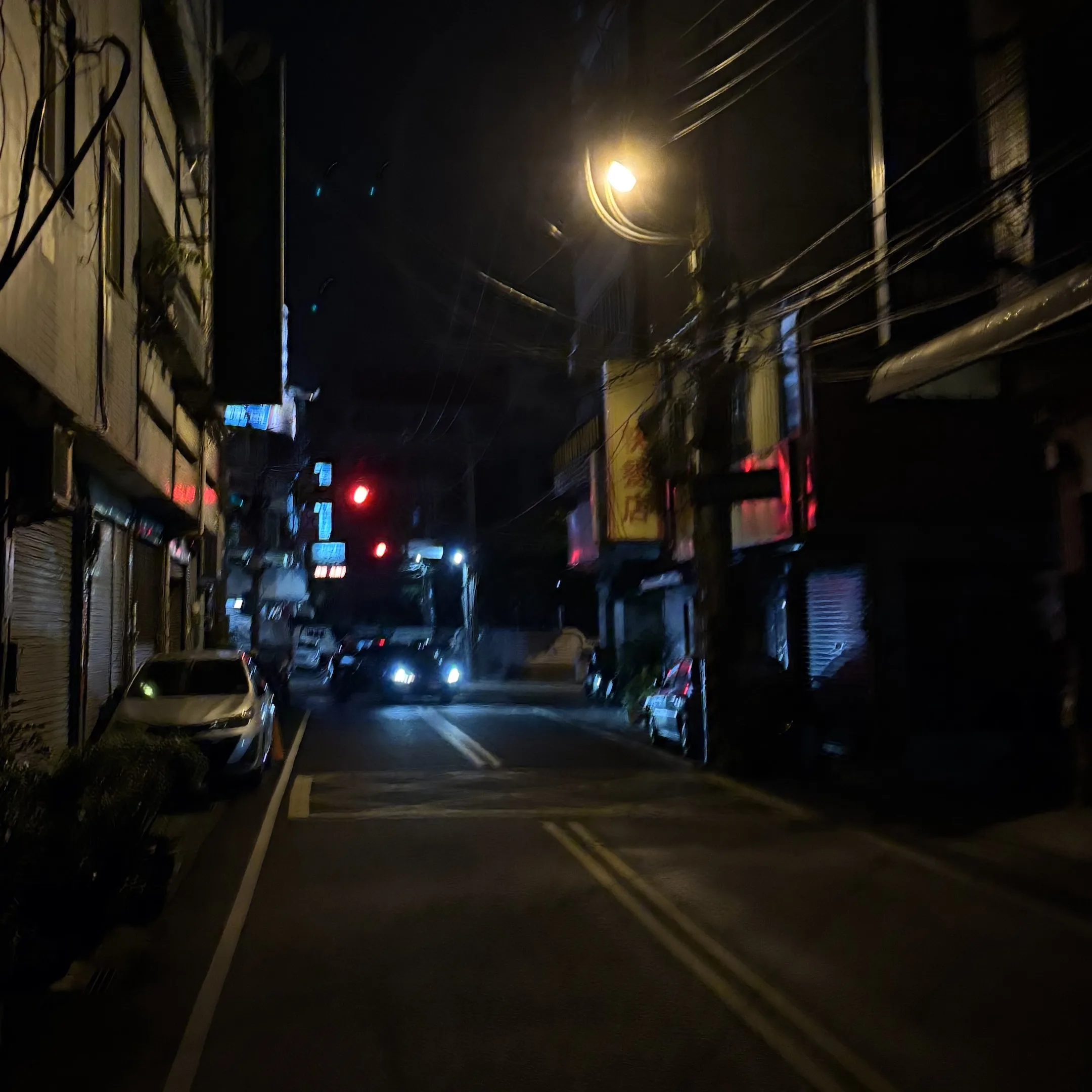 A street at night with a car driving down the street.