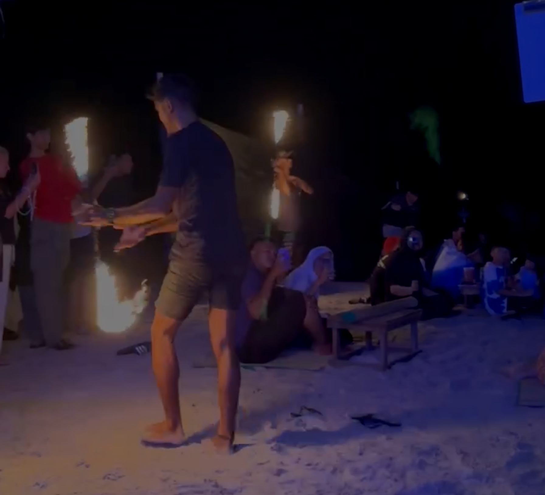 A man is standing in the sand with a fire.