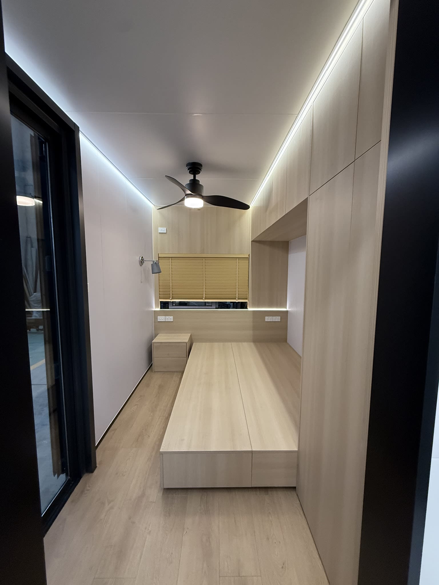 Interior of a fitted-out donga sleeping room with built-in joinery, platform bed and timber-look flooring