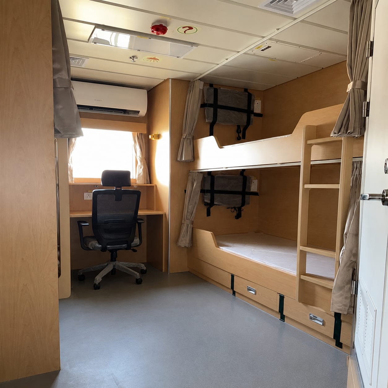 Interior of a modular accommodation unit with bunk beds, privacy curtains and a desk