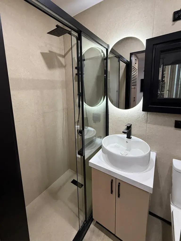 Container home bathroom with a glass shower screen, a backlit oval mirror and a basin on a timber vanity