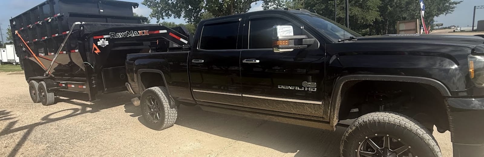 A Forging Solutions truck hauling a black roll-off dump trailer