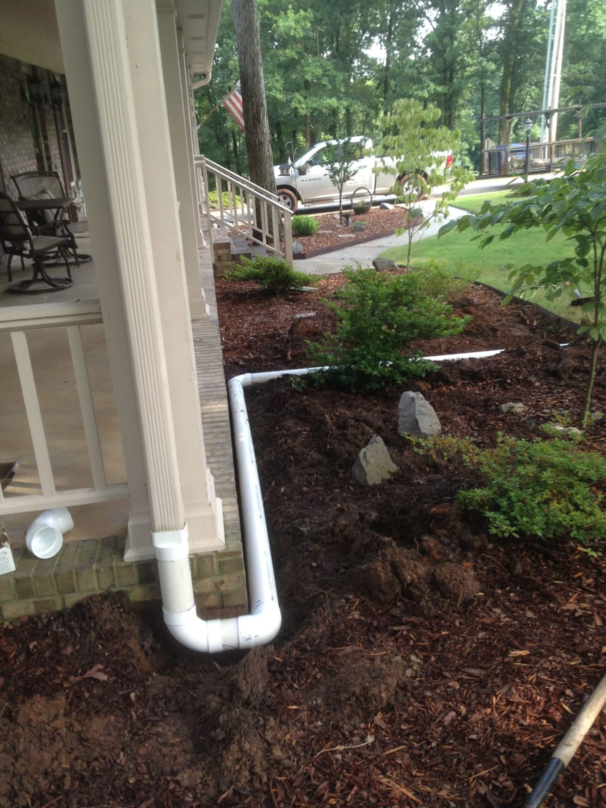 Side angle of ongoing underground drainage installation with workers fitting drain pipes in Harvest, AL