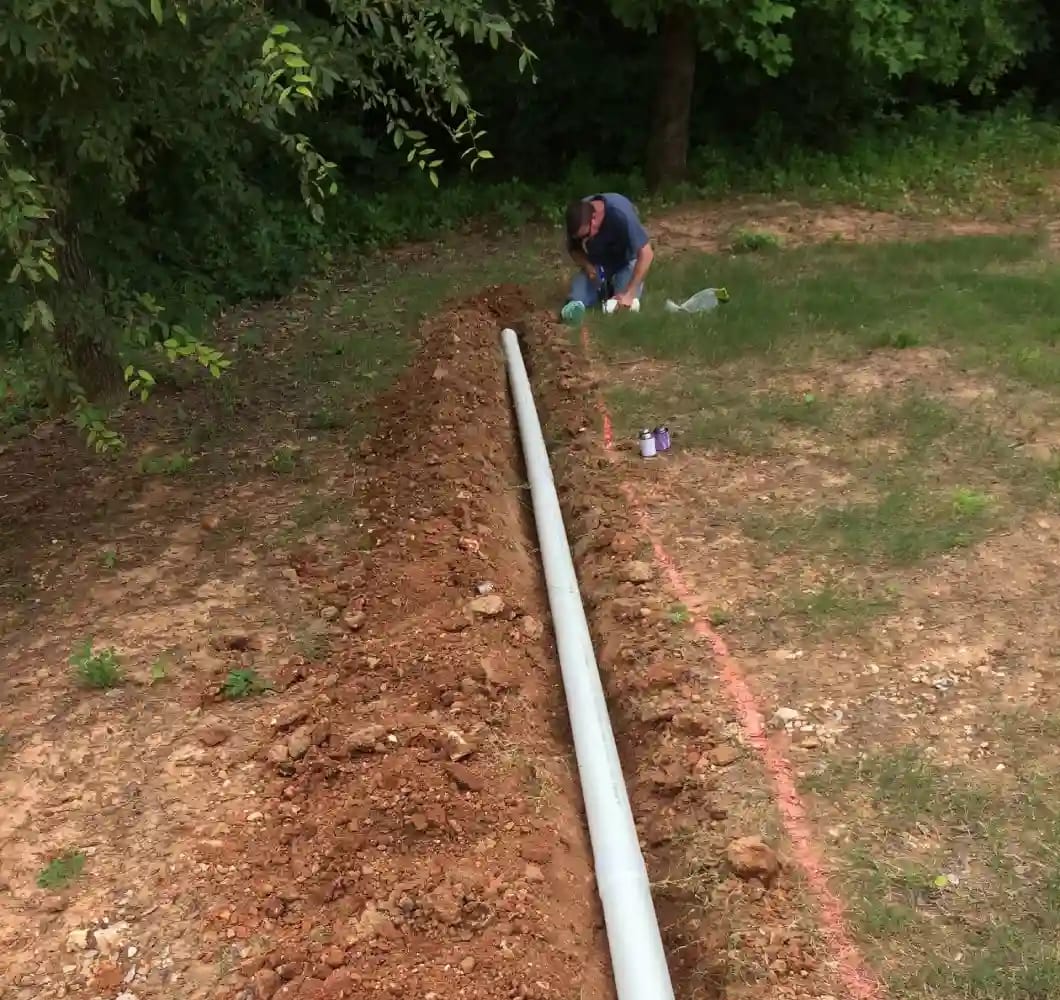Construction worker installing an underground drainage pipe in a trench at a building site in Harvest, AL