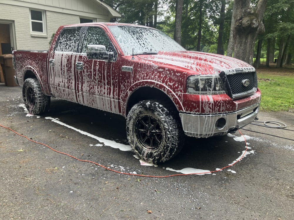 A lifted red Ford F-150 covered in wash foam during a mobile detail in a North Alabama driveway