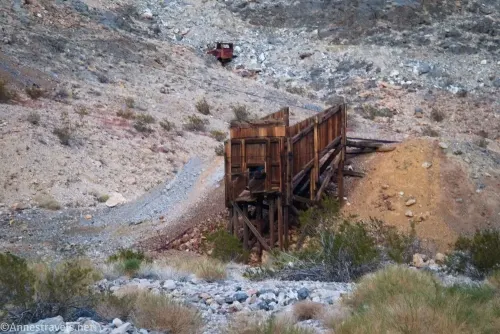 A wooden ore bin beside an orange slope on a gravel hillside 