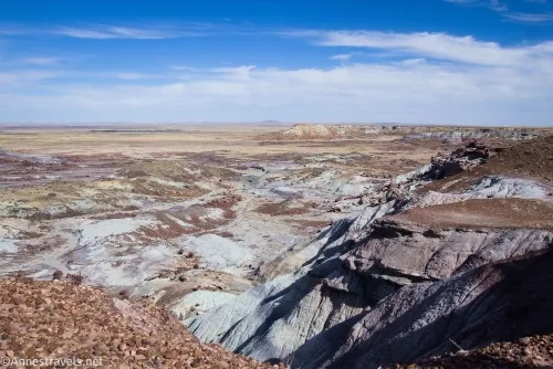 Blue sky with clouds above a tan plain and a maze of white and red washes and badlands