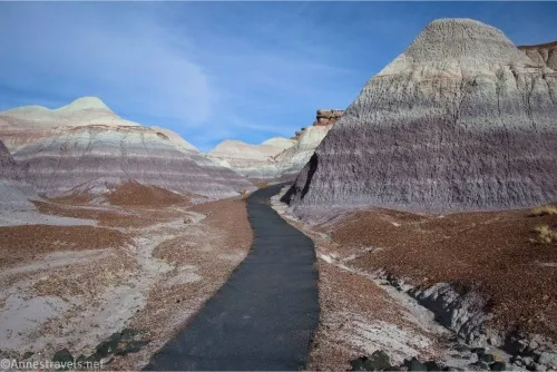 Blue skies above striped blue, red, and white badlands with a black paved trail