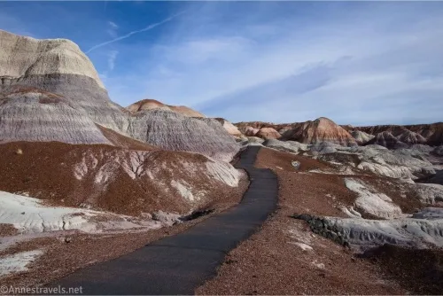 Below purple badlands, a black paved trail travels among red gravel