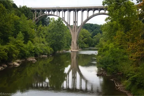 A large and delicately curved bridge is reflected in the river below
